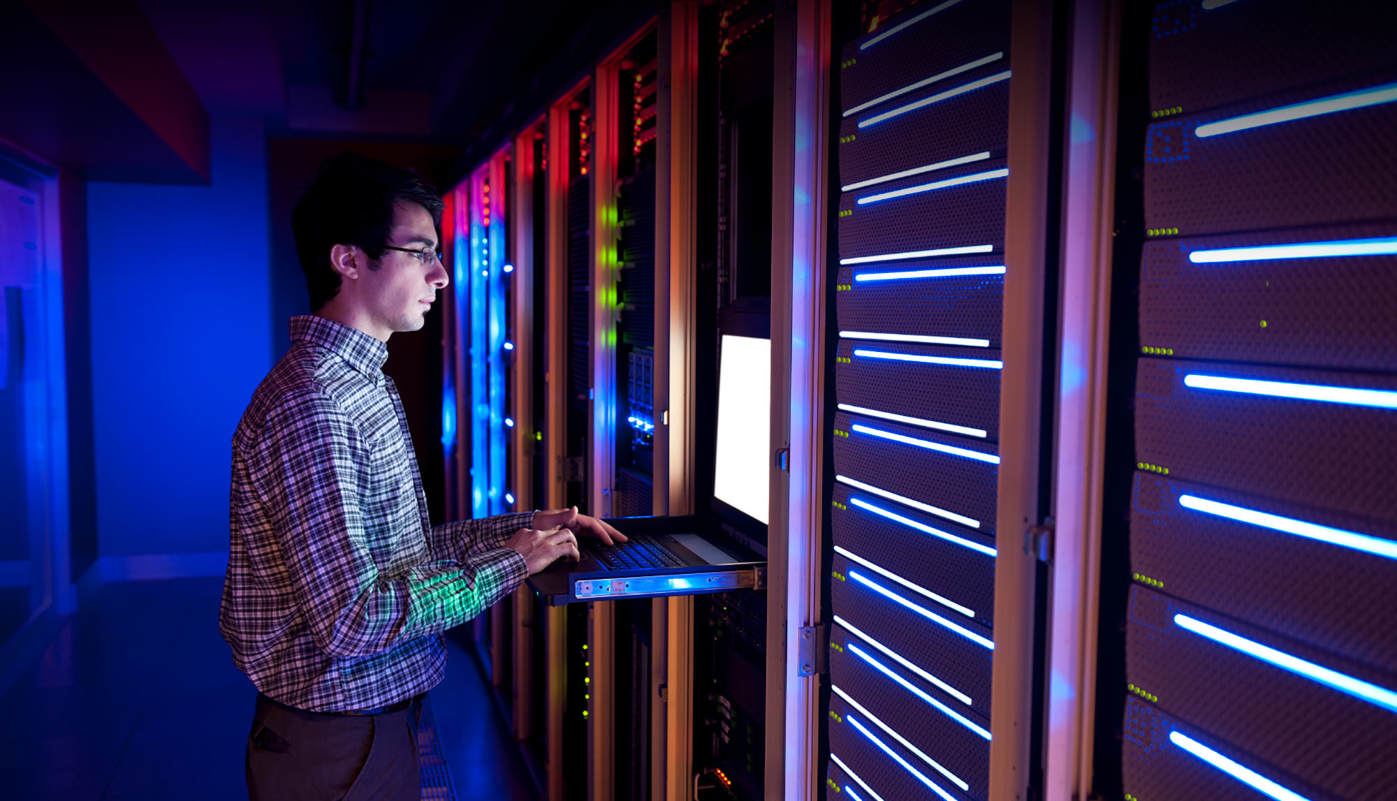 IT-Techniker arbeitet an leuchtenden Serverracks in blau illuminiertem Rechenzentrum